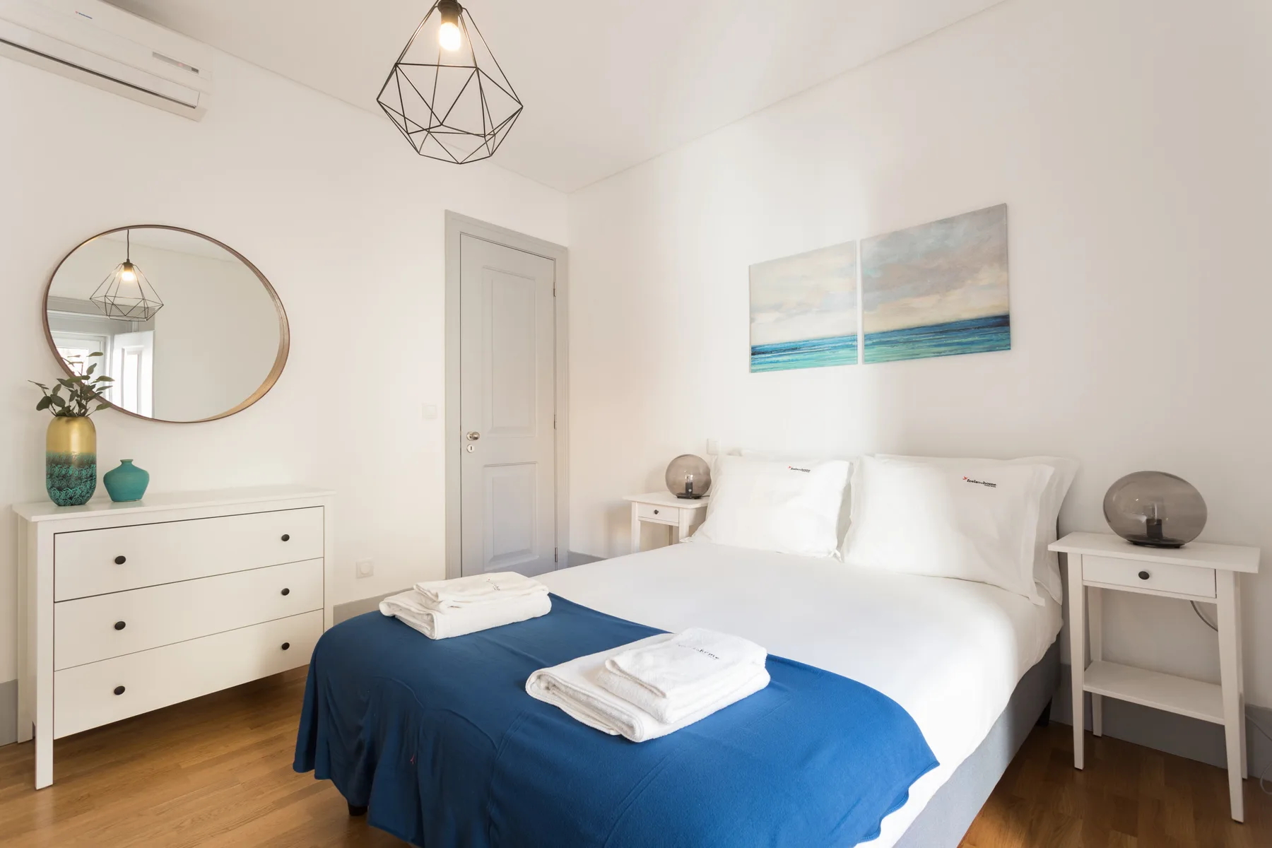 Un dormitorio luminoso con una cama doble vestida de blanco y azul.