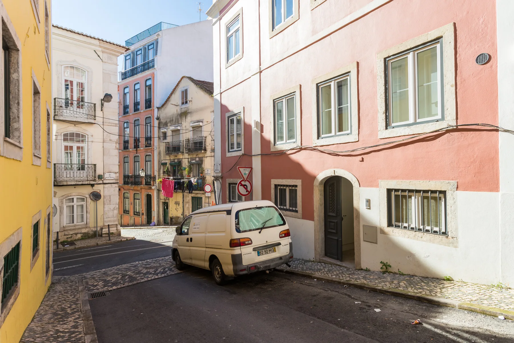 Una calle estrecha de la ciudad flanqueada por edificios de colores pastel y coches aparcados.