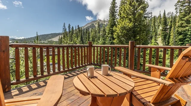 A wooden deck with outdoor seating overlooks a forested mountain landscape.