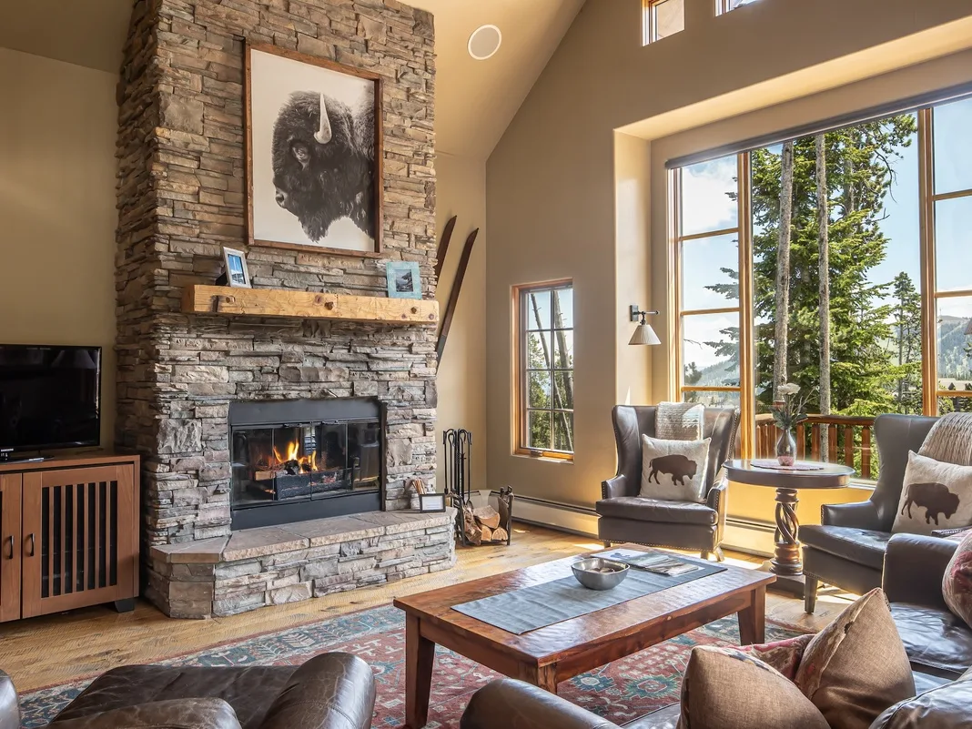 Una sala de estar con chimenea de piedra, asientos y grandes ventanas.