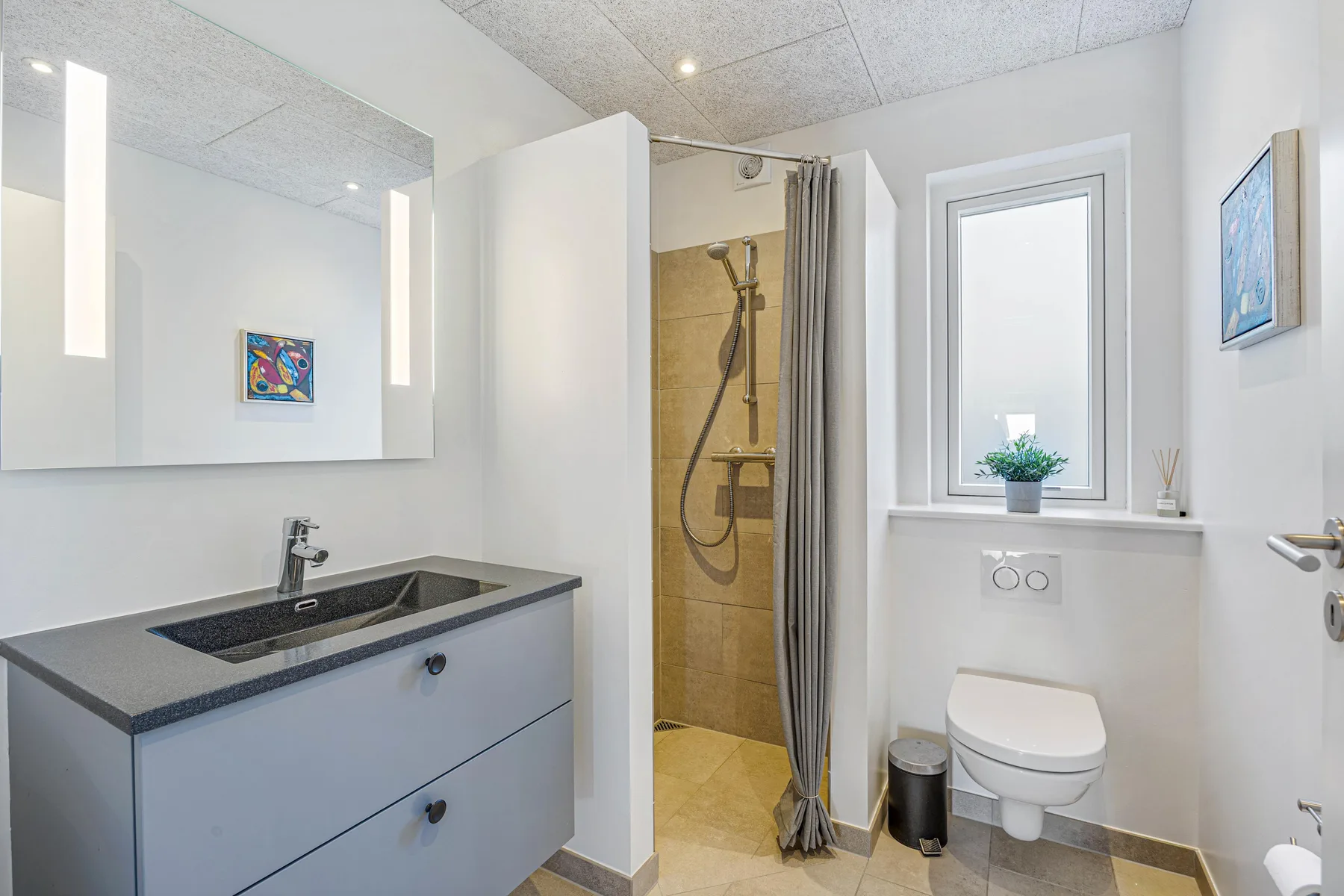Un baño luminoso con tocador, espejo y ducha con cortina.