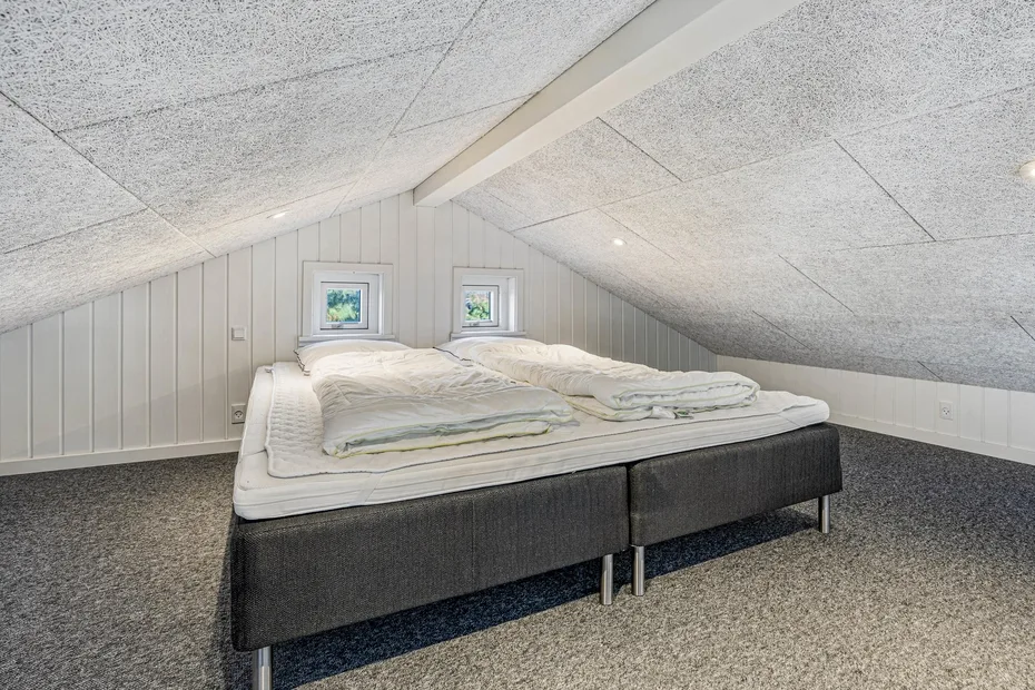Una cama con ropa de cama blanca está bajo un techo inclinado en un dormitorio.