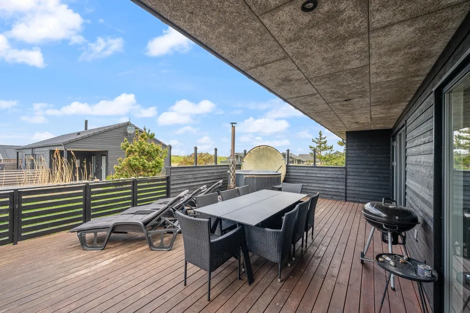 Una terraza exterior cubierta tiene una mesa de comedor y asientos.