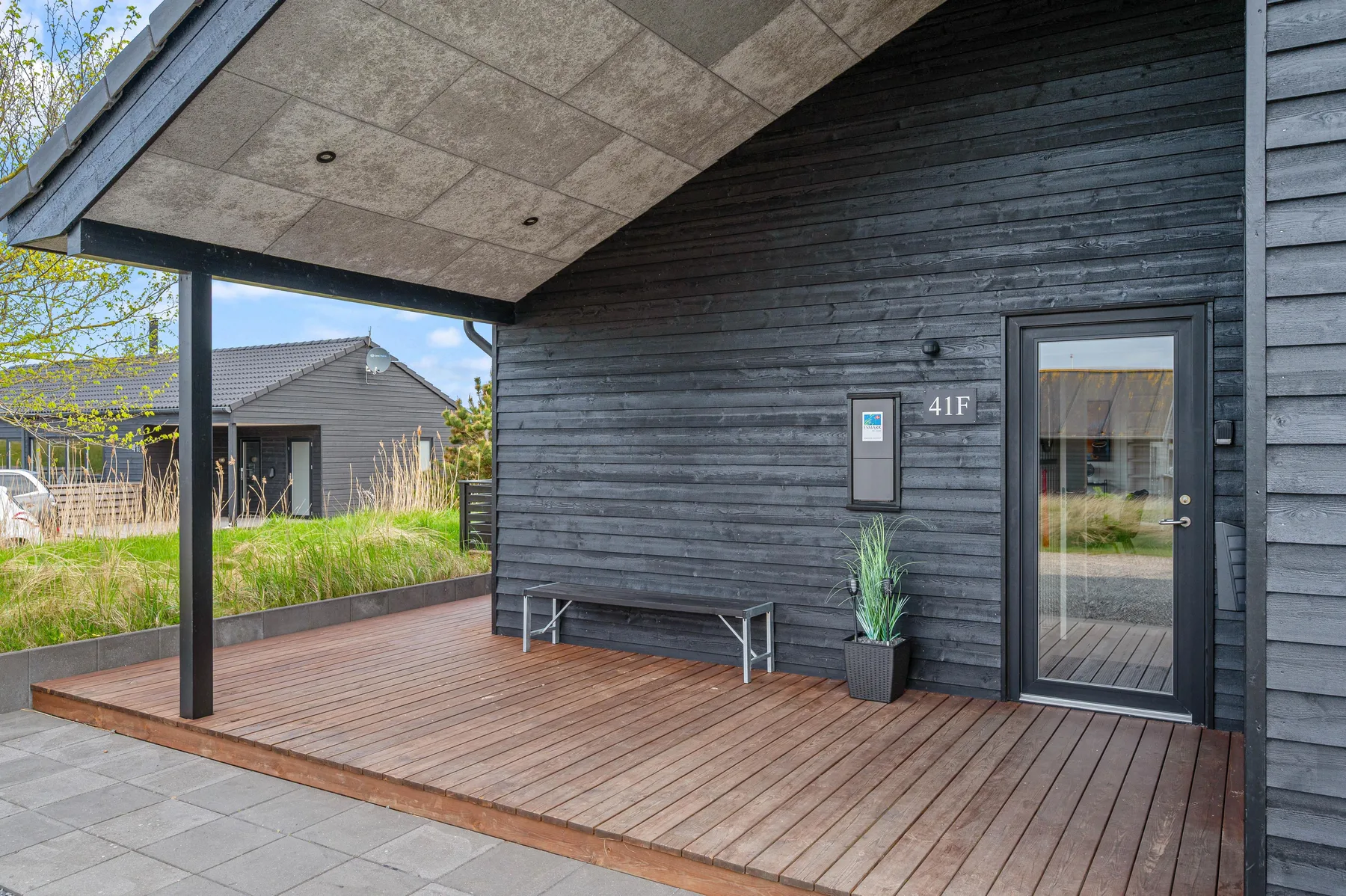 Una terraza exterior cubierta con revestimiento oscuro, un banco y una puerta de vidrio.