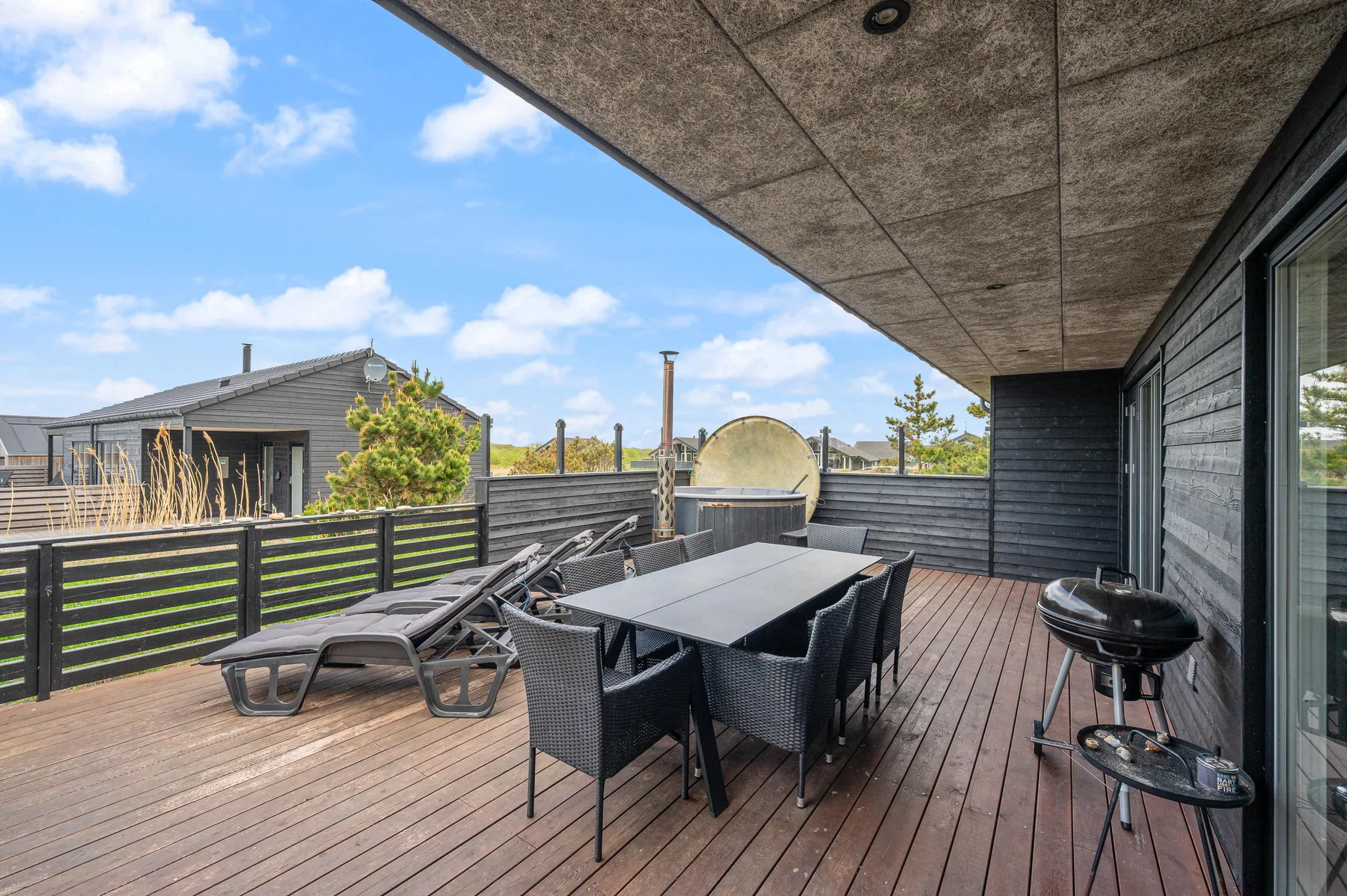 Una terraza exterior cubierta tiene una mesa de comedor, asientos y una parrilla.