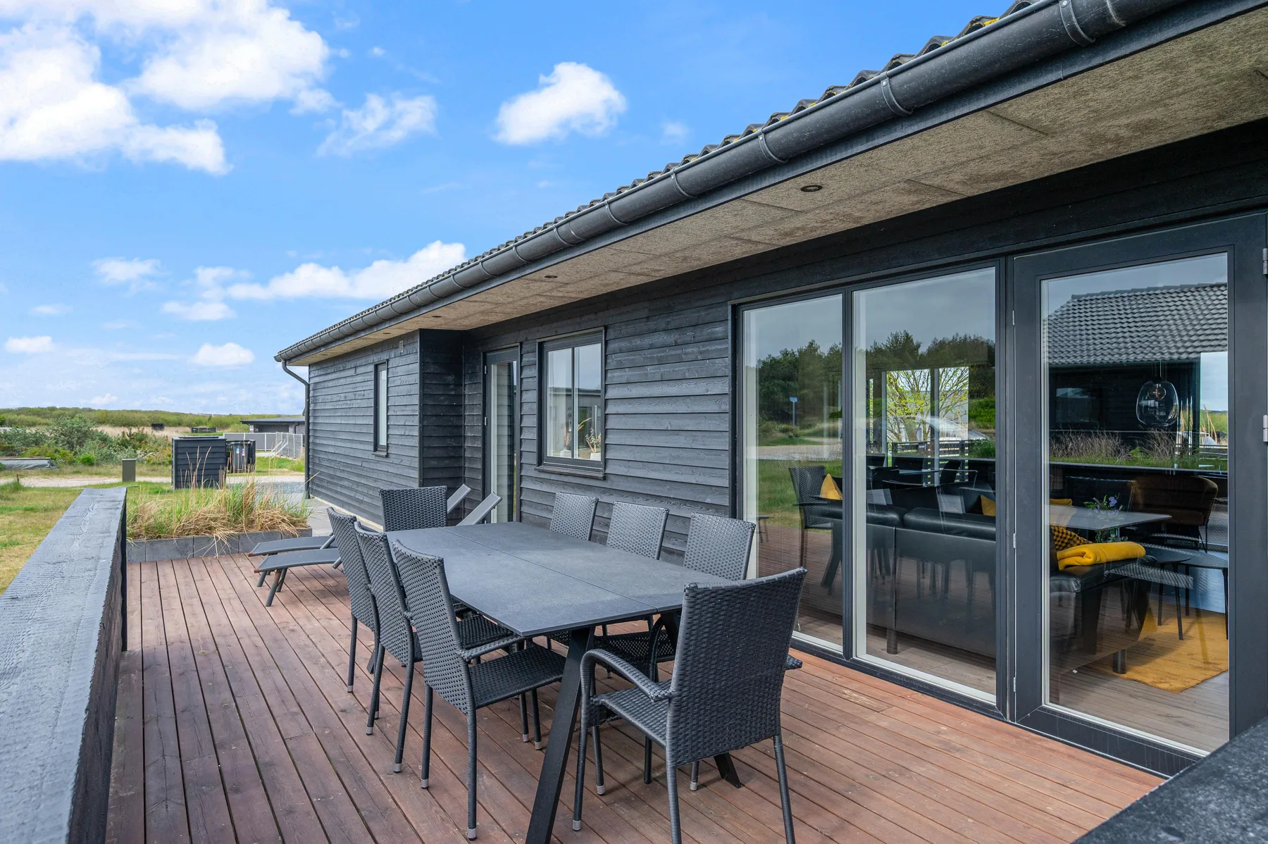 Una terraza de madera con muebles de comedor al aire libre junto a una casa moderna.