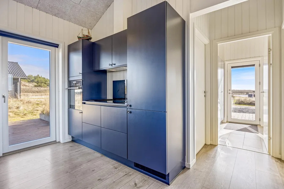 Una cocina compacta con gabinetes oscuros está junto a una entrada luminosa.