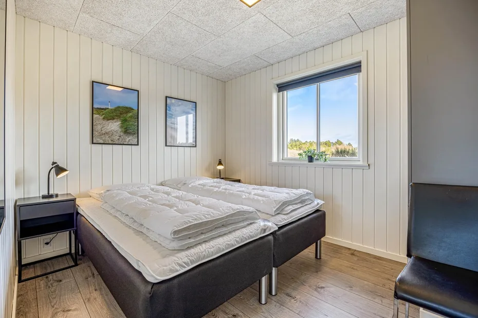 Un dormitorio con dos camas, cuadros enmarcados y una ventana con vista a los árboles.