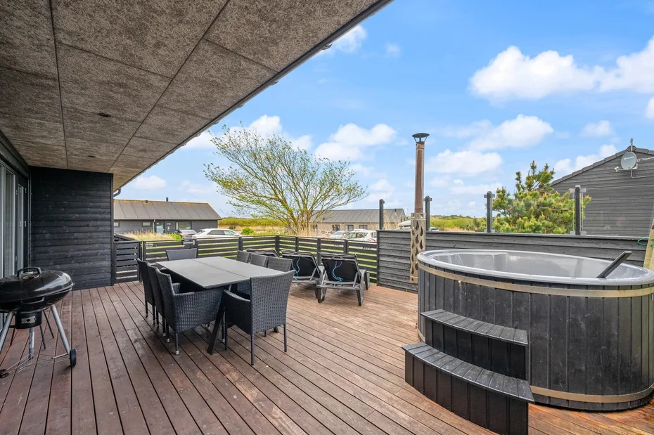 Una terraza exterior tiene un comedor y una gran bañera de hidromasaje redonda.