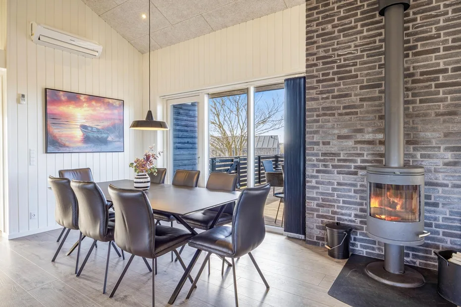 Un comedor con una mesa y asientos junto a una chimenea de ladrillo y puertas de vidrio.
