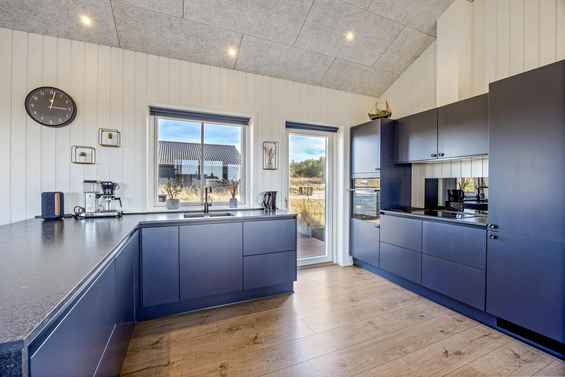 Una cocina moderna con gabinetes oscuros, una isla central y ventanas grandes.