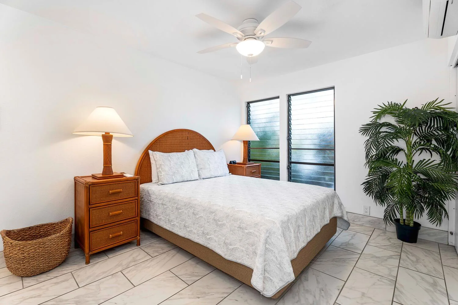 Un dormitorio luminoso con una cama, mesitas de noche y ventanas grandes.