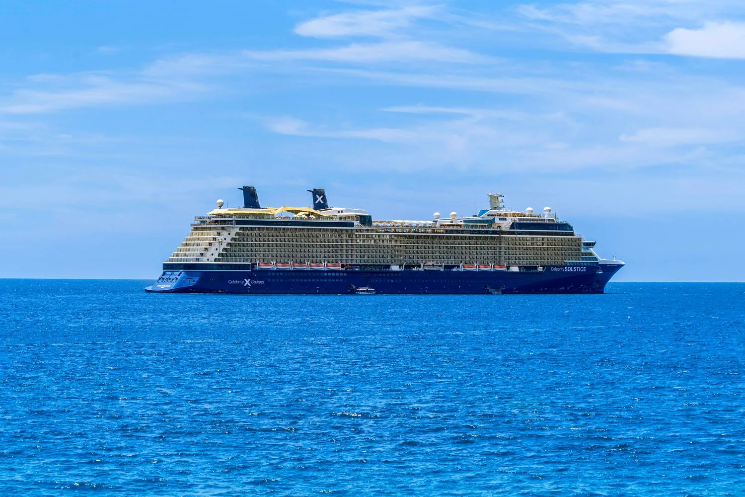 Un gran crucero navega por el mar azul bajo un cielo despejado.