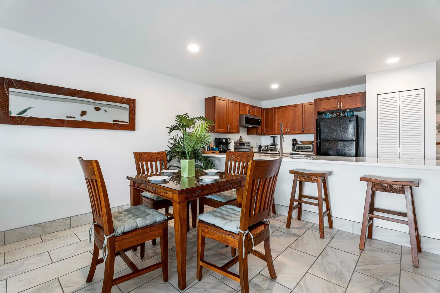 Un comedor se abre a una cocina con gabinetes de madera y una barra.