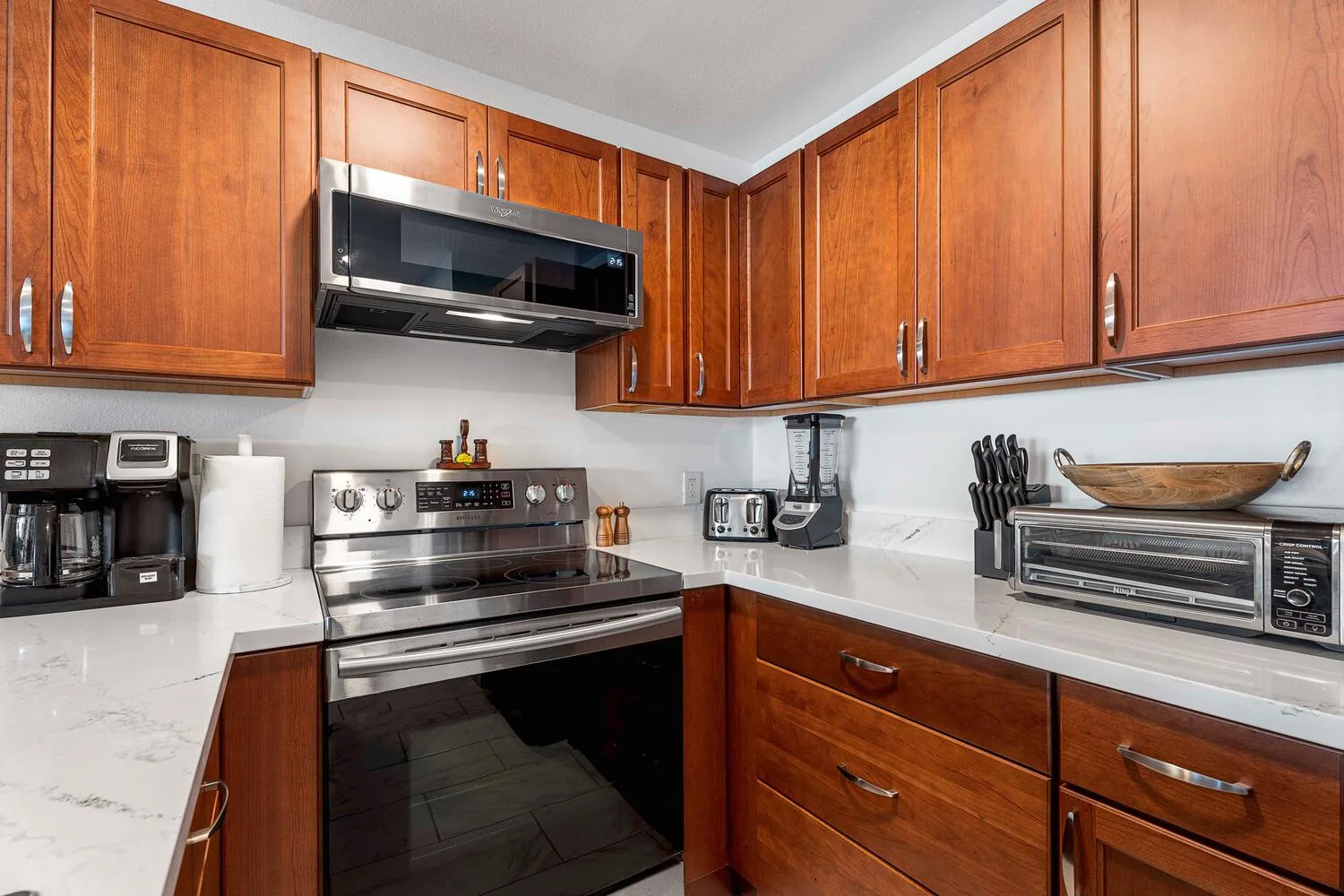 Una cocina con gabinetes de madera, encimeras blancas y electrodomésticos de acero inoxidable.