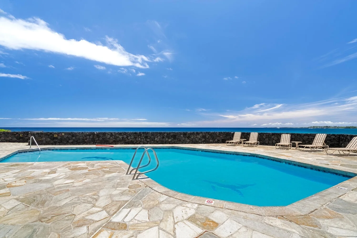 Una piscina con pavimento de piedra y tumbonas junto al mar.