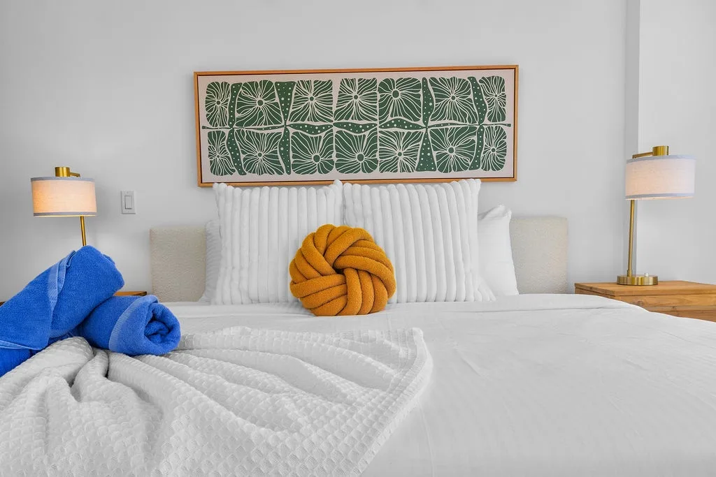 Your stylish retreat awaits with plush bedding, tropical botanical artwork, and modern bedside lamps that create a serene, restful atmosphere.