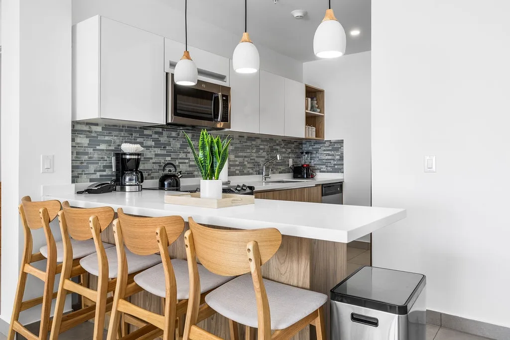 Gather around this sleek kitchen island where morning coffee and evening meals become effortless. Crisp white countertops, modern appliances, and warm pendant lighting create your home-away-from-home for every culinary moment.