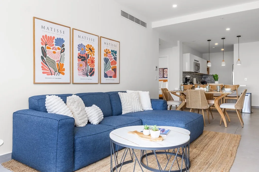 Settle into your open-concept living space featuring colorful Matisse artwork, a plush blue sofa, and an inviting dining area perfect for shared meals.