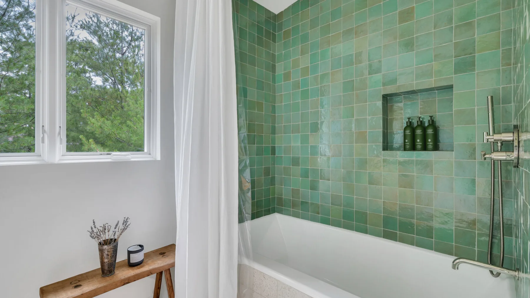 Un baño con bañera, paredes de azulejos verdes y una ventana.