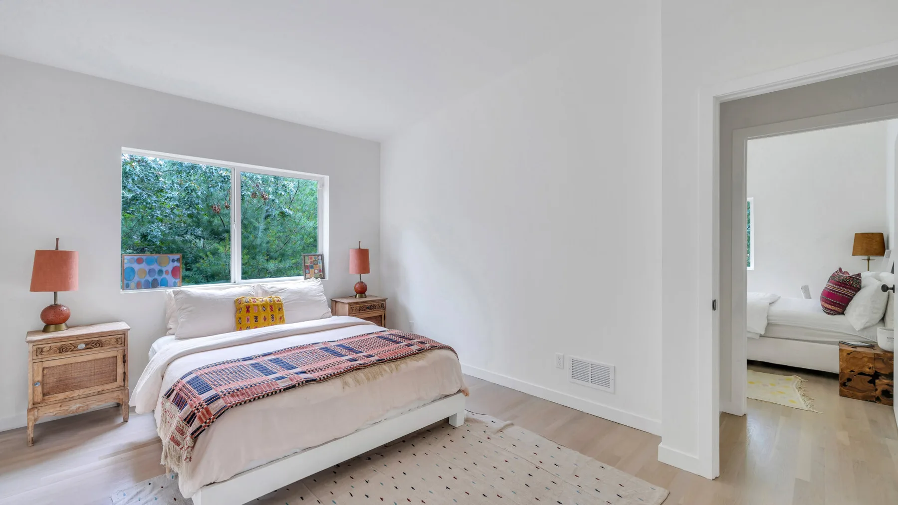 Un dormitorio luminoso con una cama tendida bajo una ventana grande.