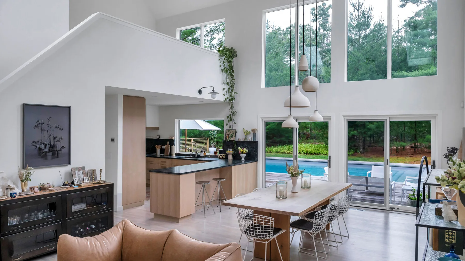 Una luminosa sala de estar y comedor diáfana da a una piscina a través de grandes ventanales.