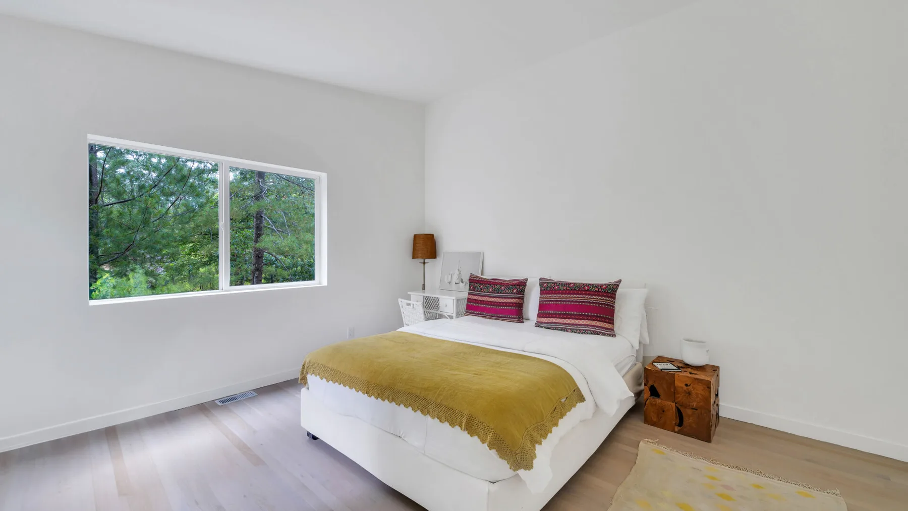 Un dormitorio luminoso con una cama vestida de blanco y una colcha color mostaza.