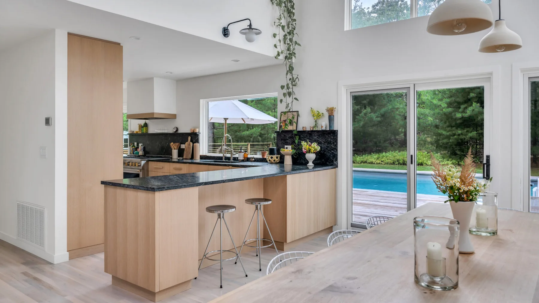 Cocina abierta y comedor con barra, mesa y ventanas con vista a una piscina.