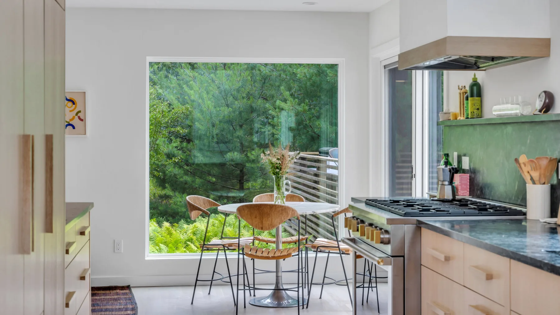 Una cocina luminosa con una mesa de comedor junto a una gran ventana con vistas a la vegetación.