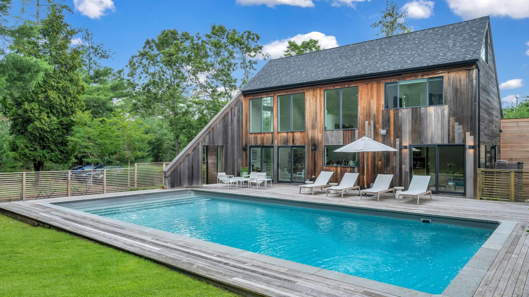 Una piscina y una terraza están junto a una casa moderna revestida de madera.