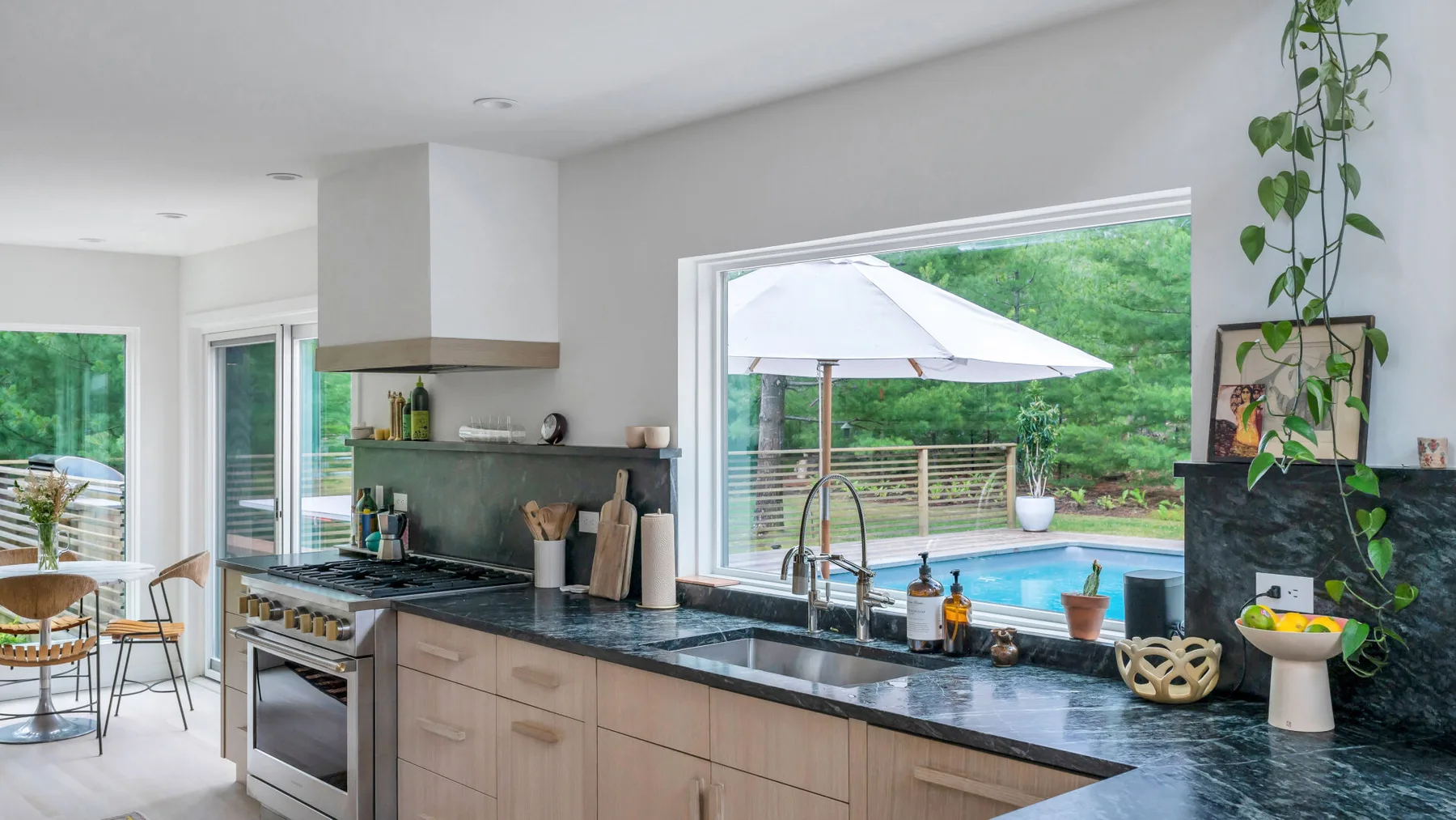 Una cocina luminosa con una encimera oscura y una ventana grande con vista a una piscina.