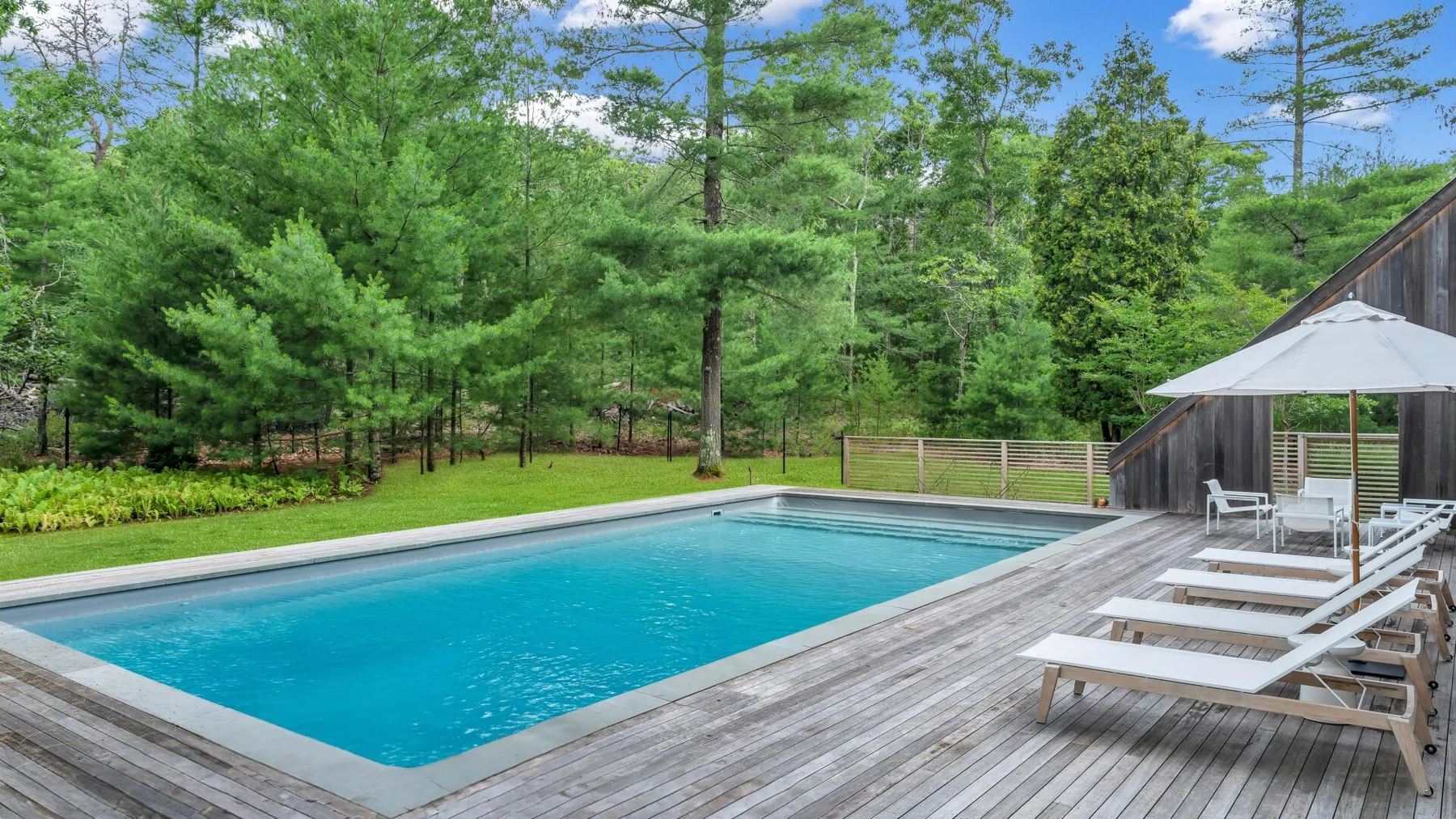 Una piscina al aire libre junto a una terraza de madera, con árboles al fondo.