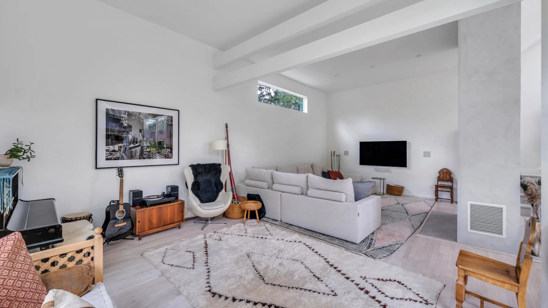 Una sala luminosa con una zona de estar, televisor y alfombra estampada.