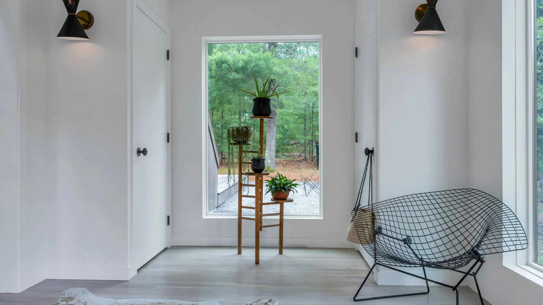 Una habitación luminosa tiene una ventana grande y un asiento colgante de alambre negro.