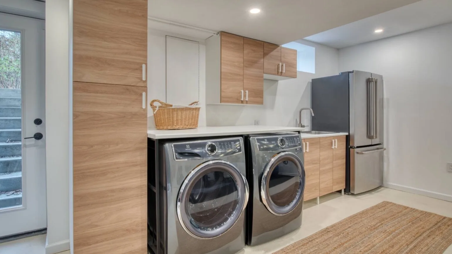 Una zona de lavandería con dos máquinas de carga frontal junto a gabinetes de madera y un refrigerador.