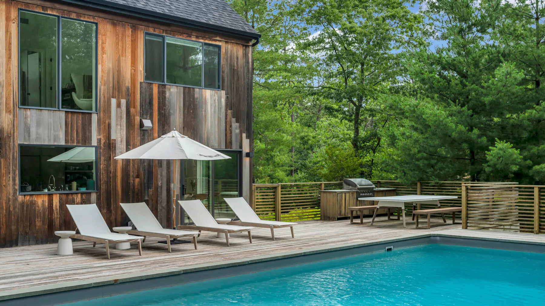 Una piscina junto a una casa de madera, con asientos de descanso en la terraza.