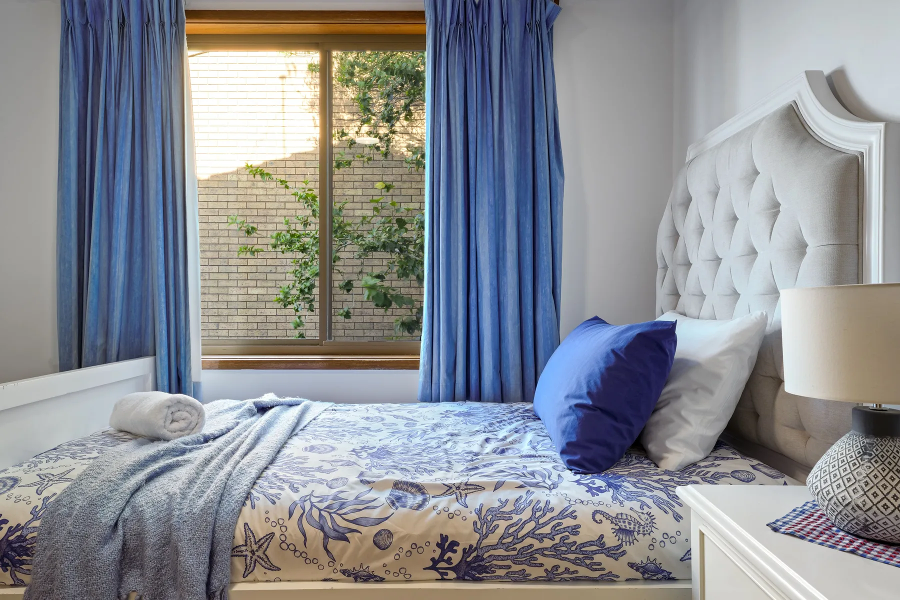 Dormitorio con una cama estampada y cortinas azules junto a una ventana.