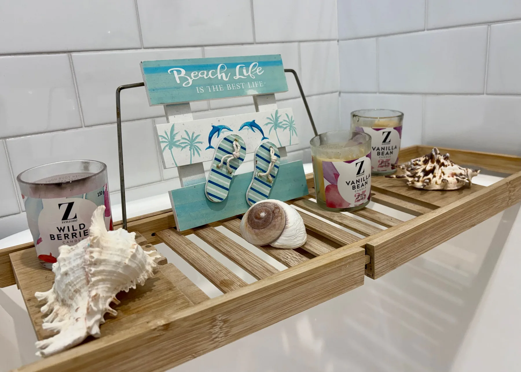 Una bandeja de madera de baño muestra conchas, velas y un letrero playero.