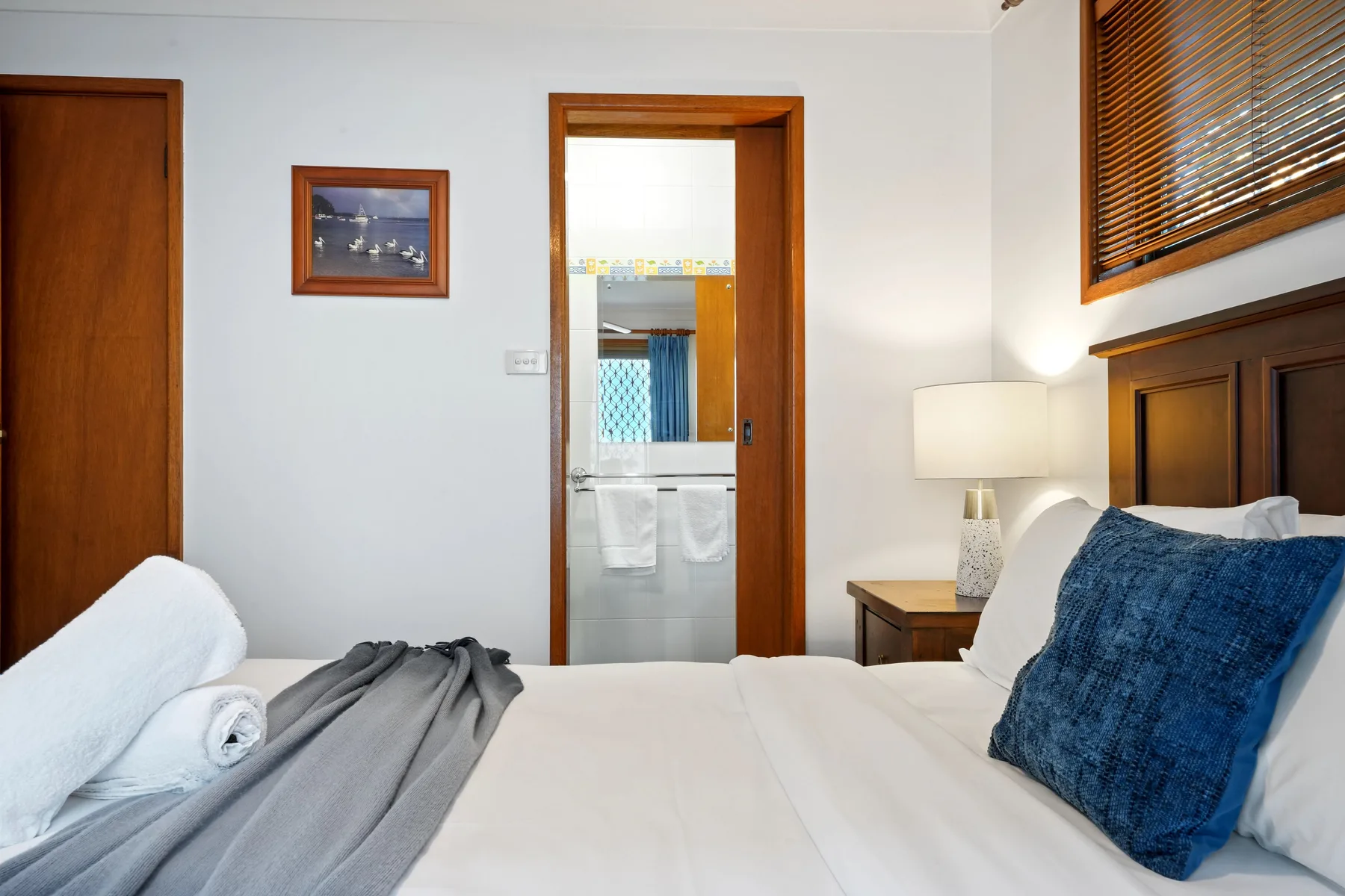 Un dormitorio con una cama bien hecha, cojines azules y una lámpara de noche.