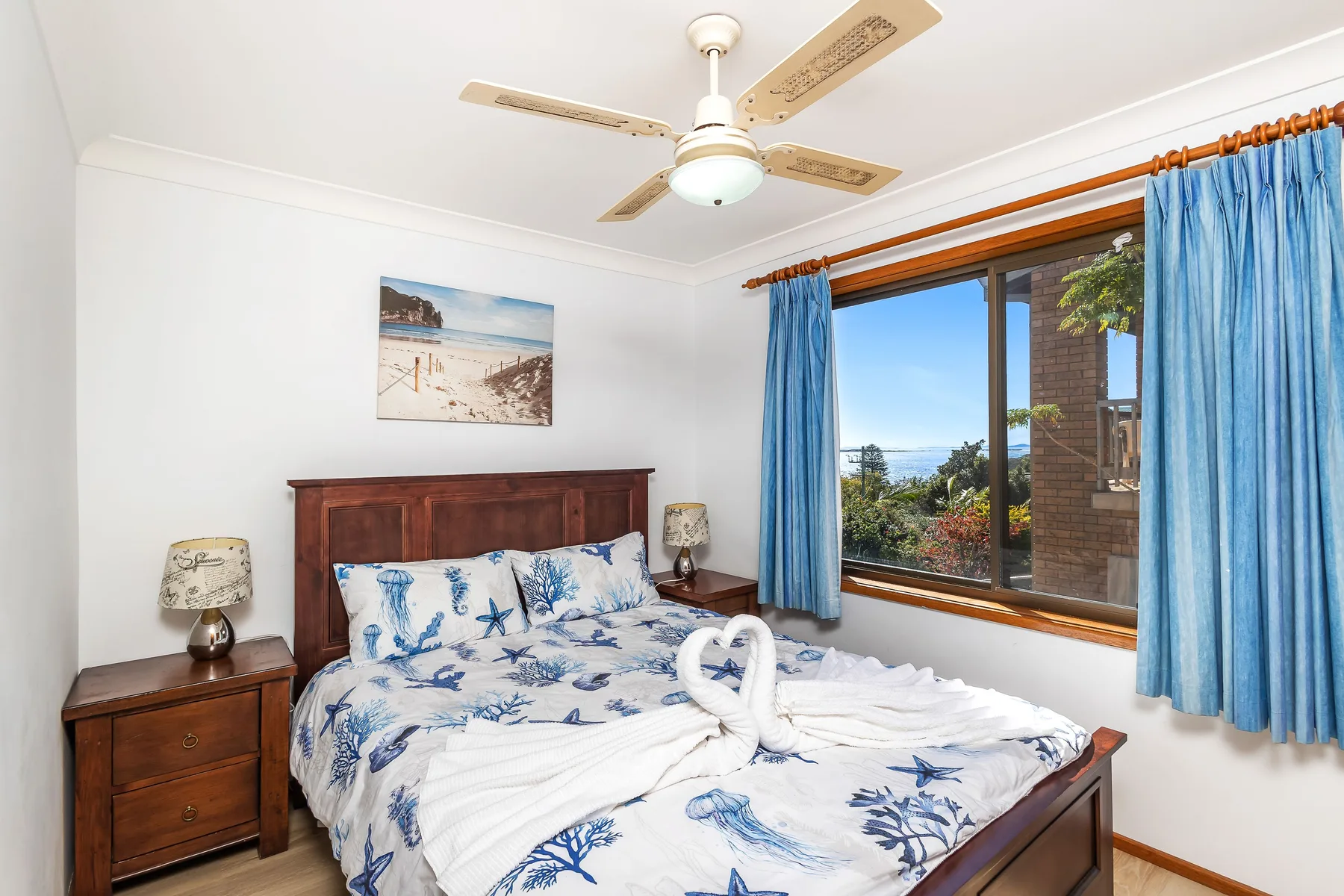 Un dormitorio con una cama de madera y cortinas azules junto a una ventana grande.