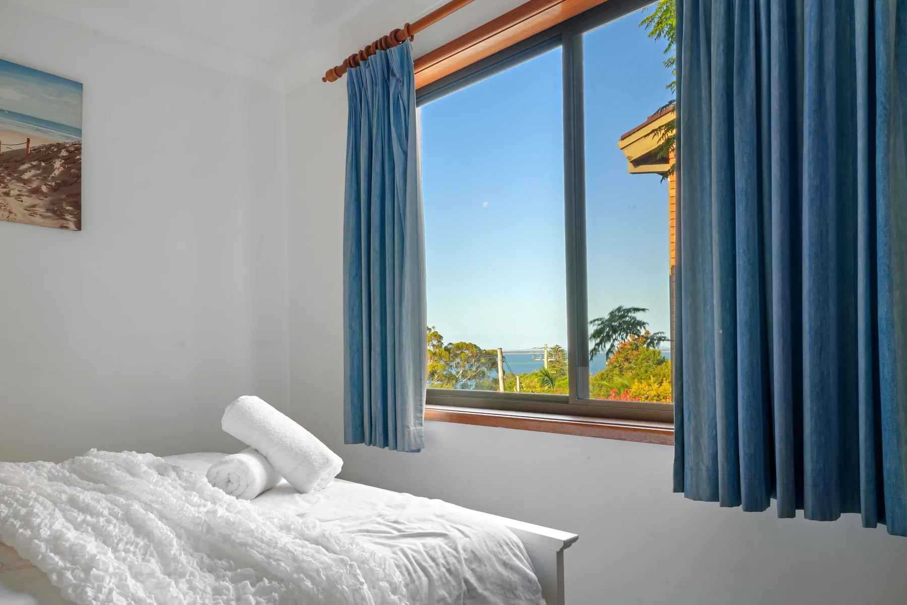 Un dormitorio con una cama junto a una ventana amplia con vistas a vegetación y agua.