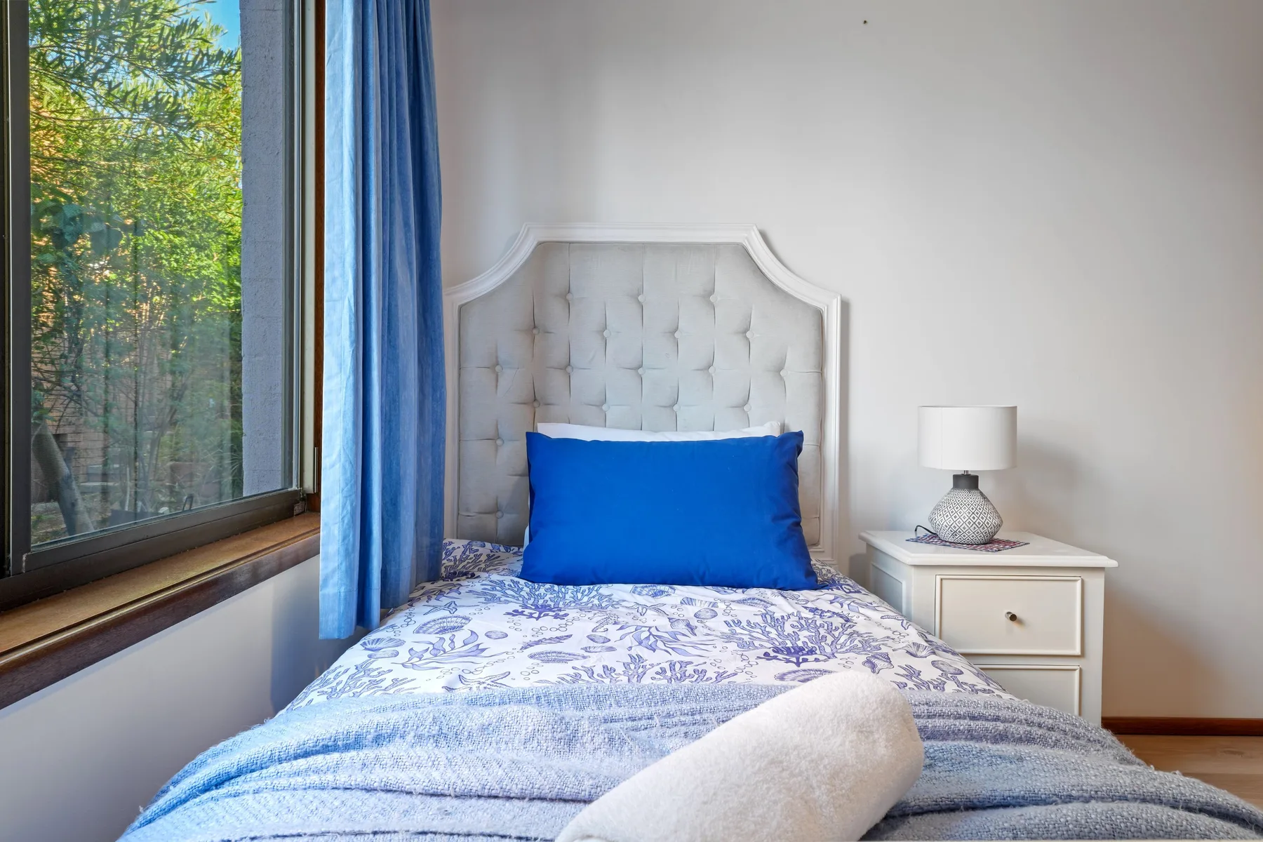 Dormitorio con una cama junto a una ventana con vista a árboles frondosos.