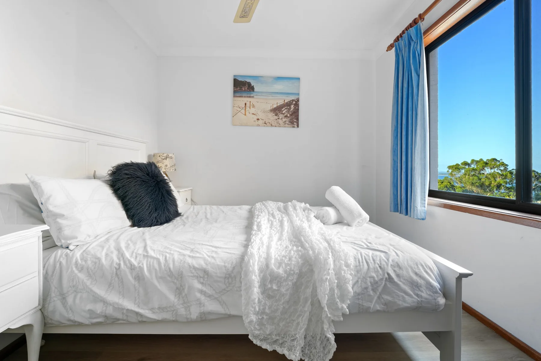 Un dormitorio luminoso con una cama blanca junto a una ventana grande.
