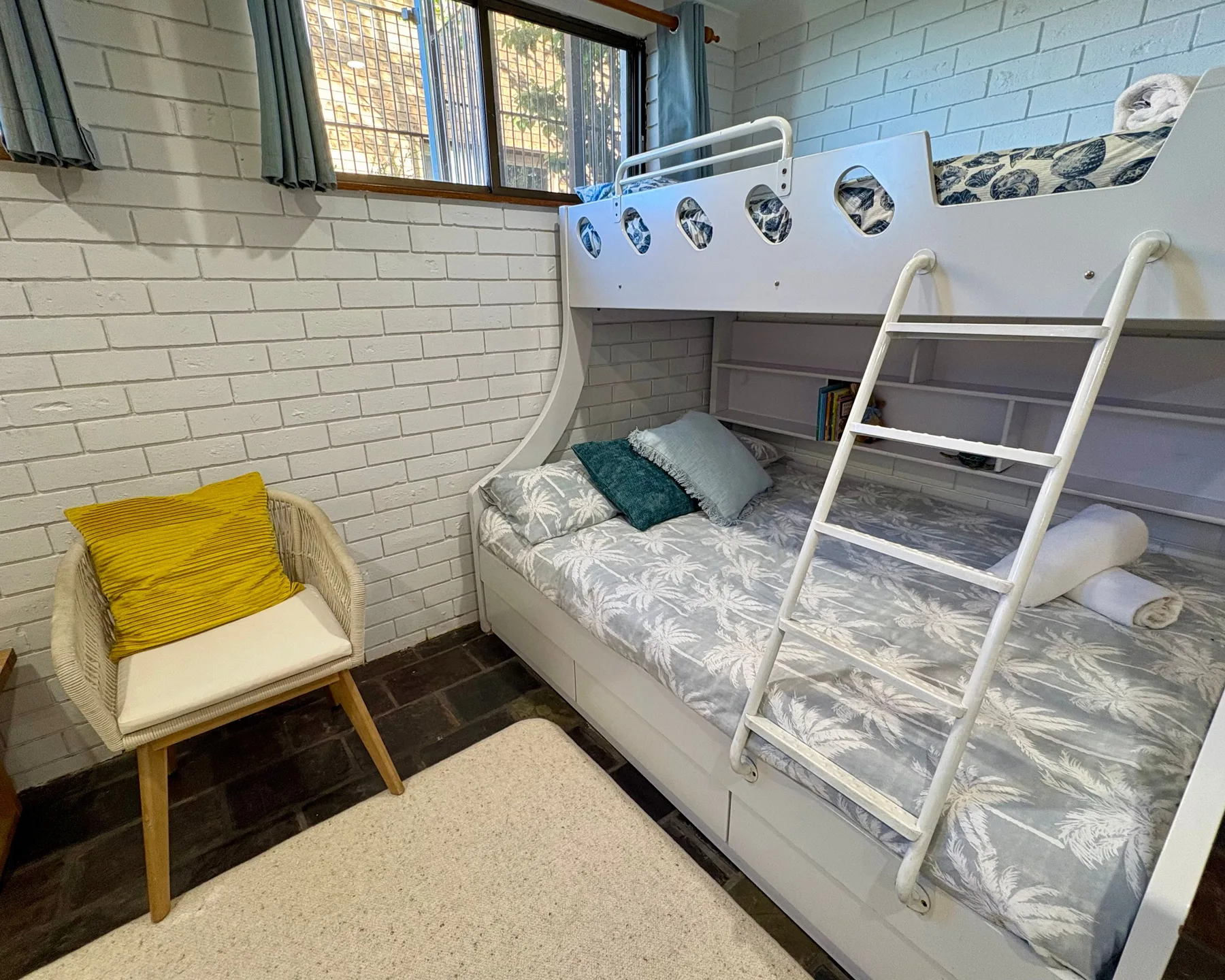 Dormitorio con litera, cama inferior y una silla junto a la ventana.