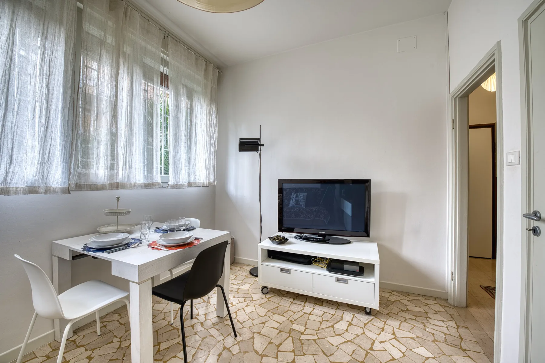 Una zona de comedor y estar con una mesa, televisión y grandes ventanas con cortinas.