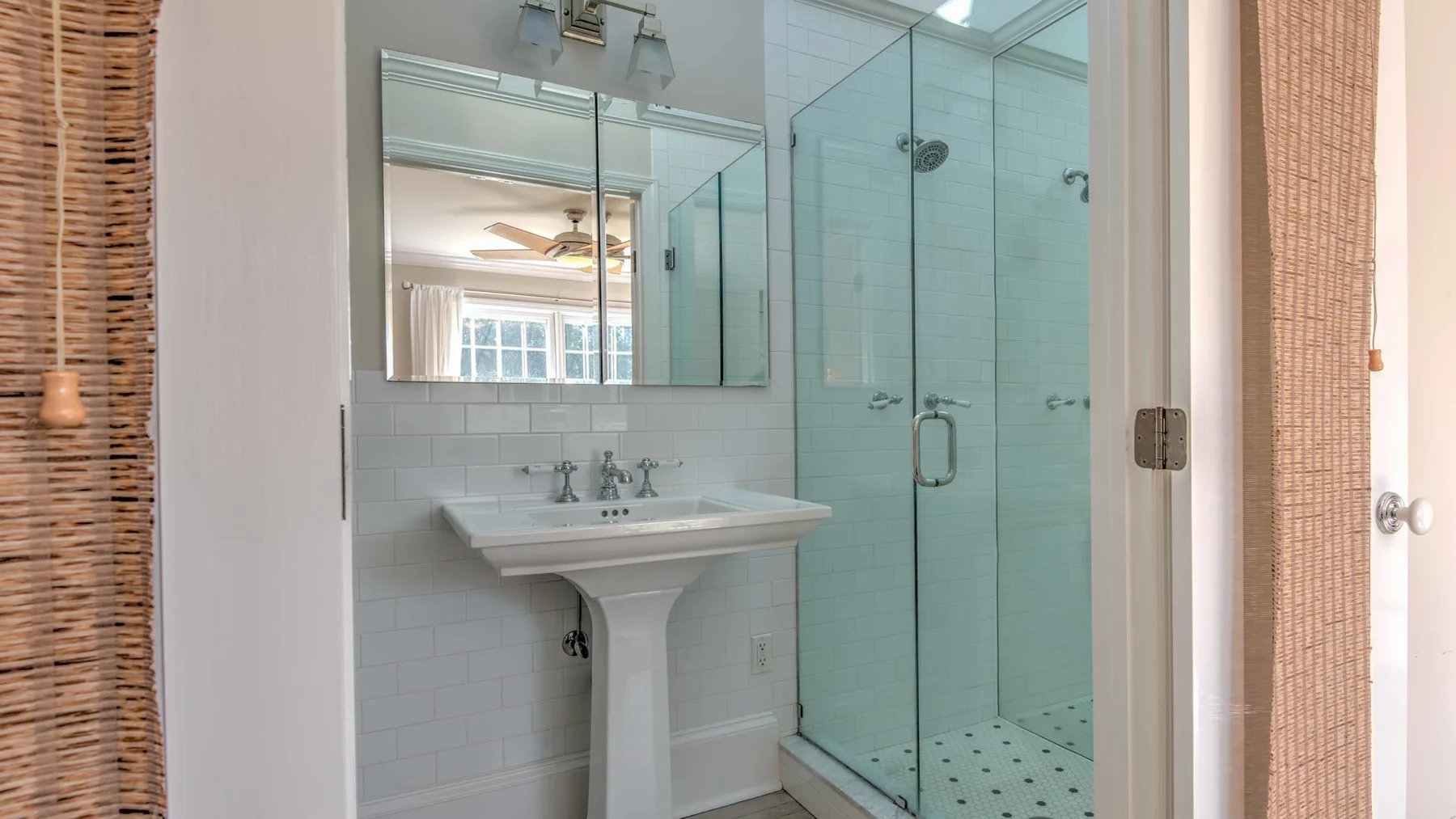 A bathroom with a pedestal sink, mirror, and glass shower.