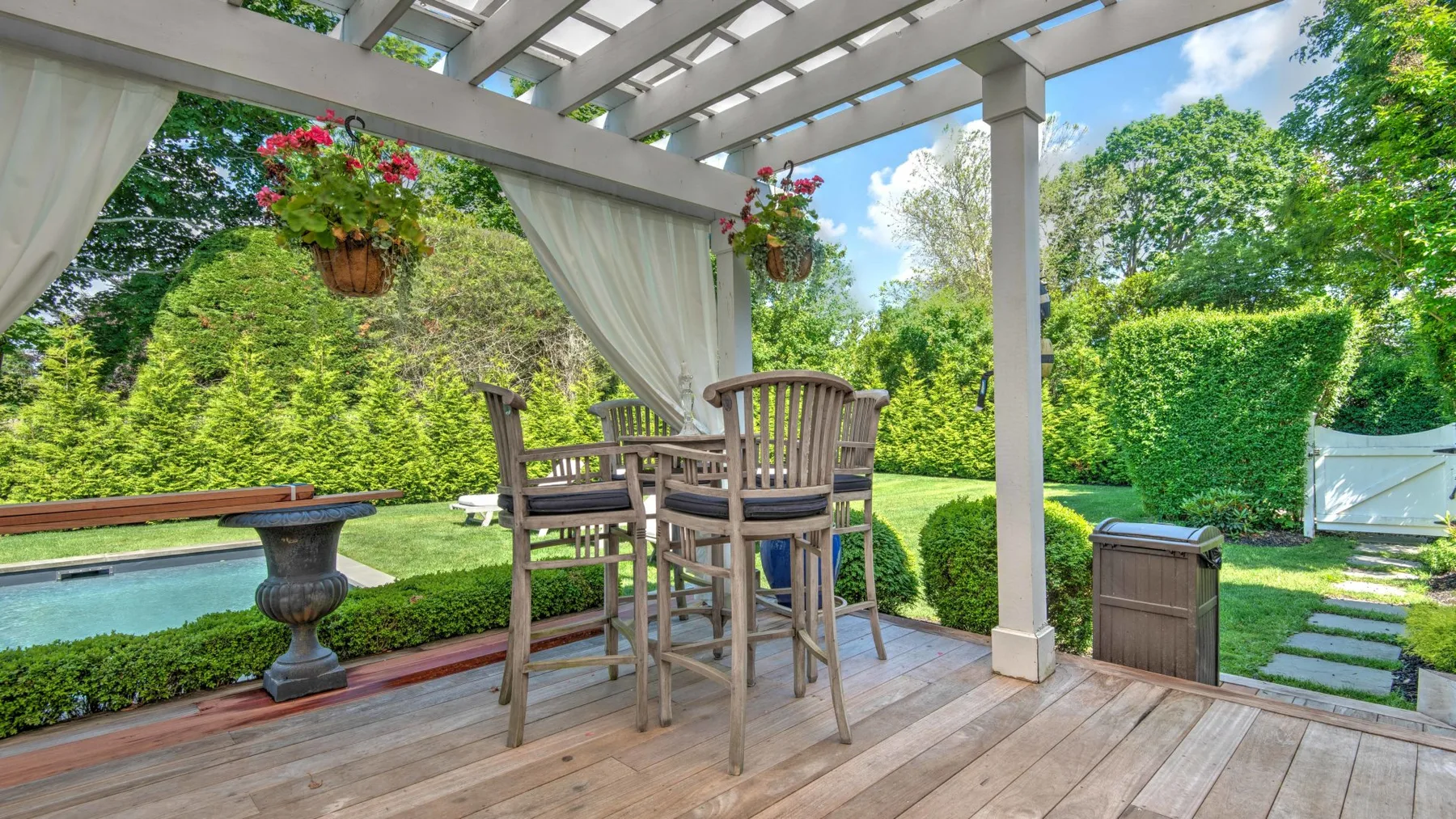 A covered outdoor patio with a dining table overlooking a garden and pool.