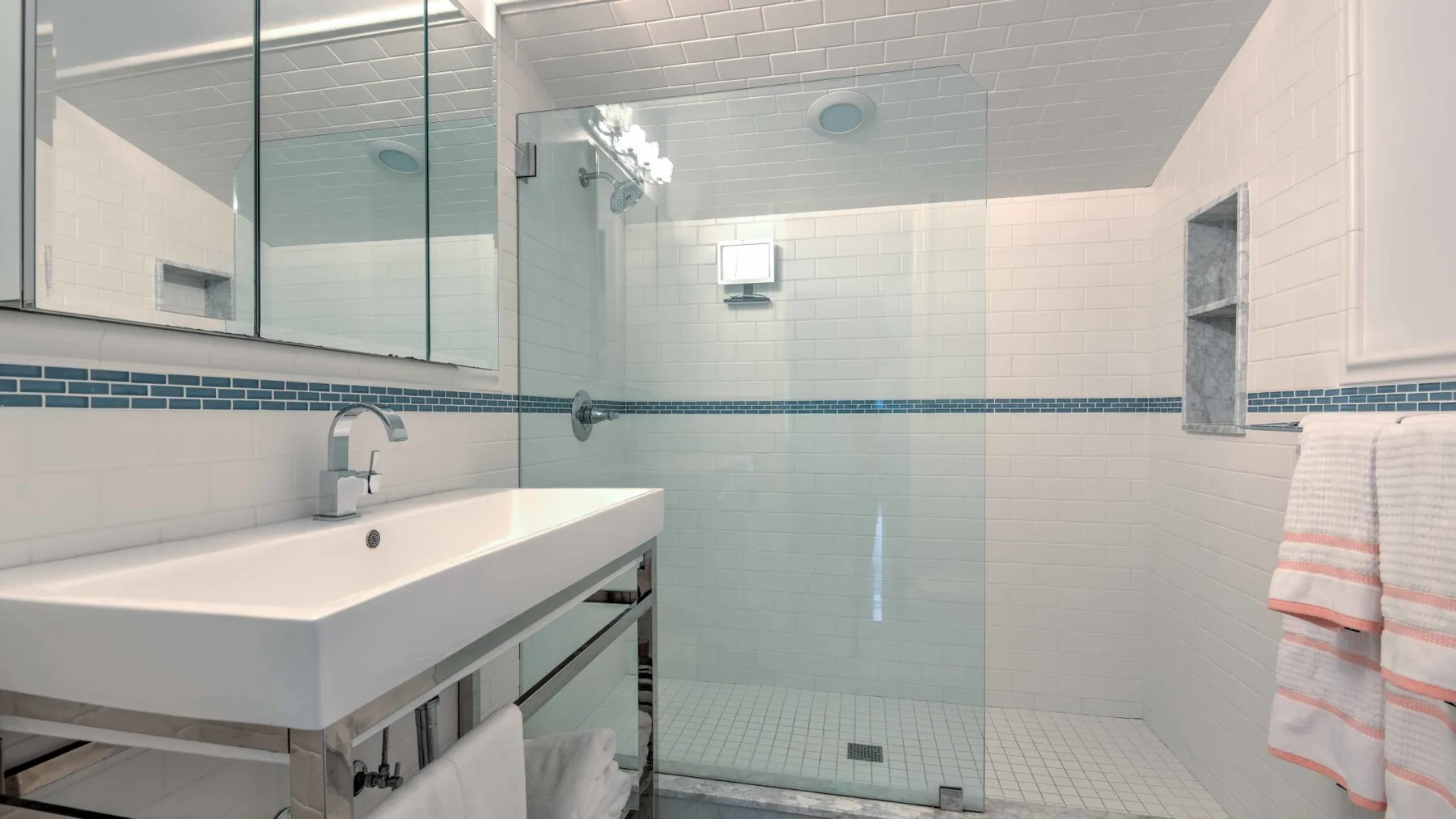 A tiled bathroom with a long sink counter and a glass shower.