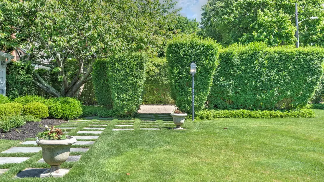 A garden lawn with stepping stones, trimmed hedges, and a small lamp post.