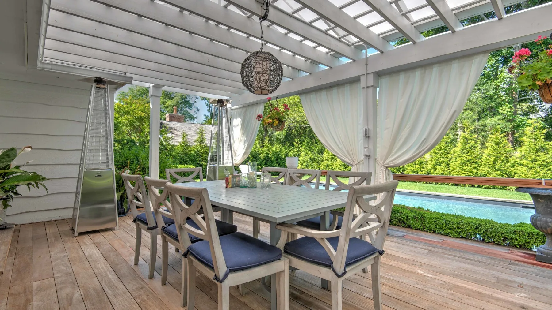 A covered outdoor dining area has a table and chairs overlooking a garden.